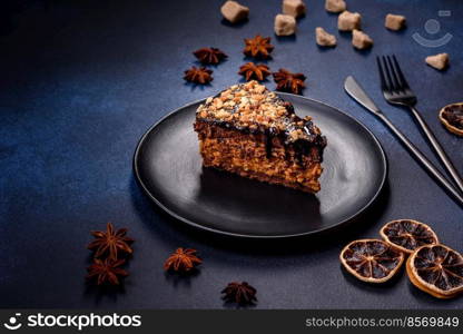 A piece of fresh delicious cake with nuts and chocolate on a black plate against a dark blue background. Desserts and sweets to the dinner table. A piece of fresh delicious cake with nuts and chocolate on a black plate against a dark blue background