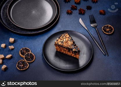 A piece of fresh delicious cake with nuts and chocolate on a black plate against a dark blue background. Desserts and sweets to the dinner table. A piece of fresh delicious cake with nuts and chocolate on a black plate against a dark blue background