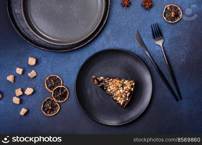 A piece of fresh delicious cake with nuts and chocolate on a black plate against a dark blue background. Desserts and sweets to the dinner table. A piece of fresh delicious cake with nuts and chocolate on a black plate against a dark blue background