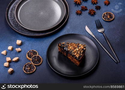 A piece of fresh delicious cake with nuts and chocolate on a black plate against a dark blue background. Desserts and sweets to the dinner table. A piece of fresh delicious cake with nuts and chocolate on a black plate against a dark blue background