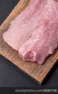 A piece of fresh juicy raw pork with salt, spices and herbs on a dark concrete background