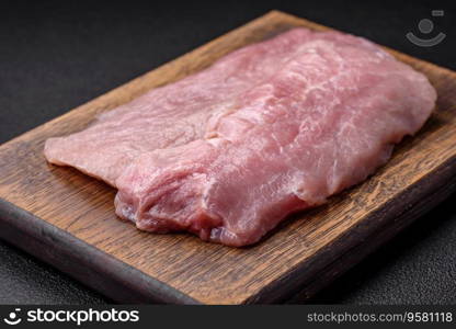 A piece of fresh juicy raw pork with salt, spices and herbs on a dark concrete background