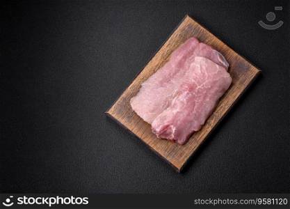 A piece of fresh juicy raw pork with salt, spices and herbs on a dark concrete background