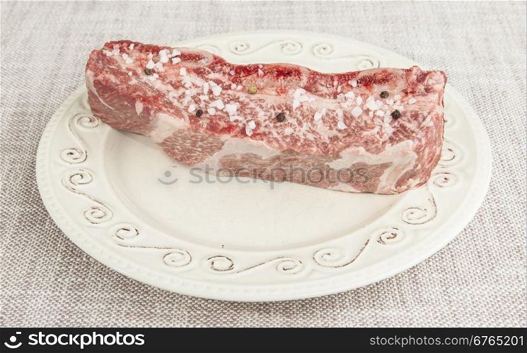 A piece of fresh marbled beef with sea salt and black pepper on the porcelain plate. A piece of fresh marbled beef with sea salt and black pepper on the porcelain plate.