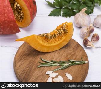 a piece of fresh pumpkin with seeds on a wooden kitchen board, behind garlic