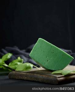 A piece of green cheese with basil on a brown wooden board, black background