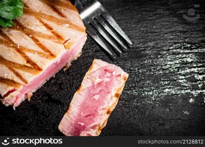 A piece of grilled tuna with parsley. On a black background. High quality photo. A piece of grilled tuna with parsley.