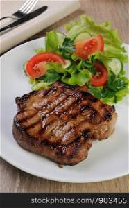 A piece of juicy pork steak grilled with a salad