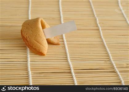 A piece of paper for a fortune displayed with a whole fortune cookie against a bamboo background