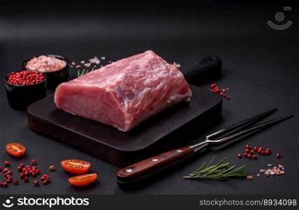 A piece of raw fresh pork on a wooden cutting board with spices and herbs on a dark concrete background