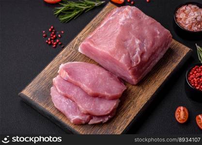 A piece of raw fresh pork on a wooden cutting board with spices and herbs on a dark concrete background