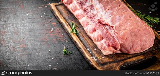 A piece of raw pork on a cutting board with a sprig of rosemary. On a rustic dark background. High quality photo. A piece of raw pork on a cutting board with a sprig of rosemary.