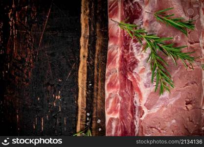 A piece of raw pork on a cutting board with a sprig of rosemary. On a rustic dark background. High quality photo. A piece of raw pork on a cutting board with a sprig of rosemary.