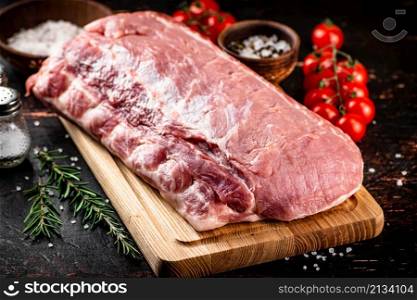 A piece of raw pork on a cutting board with tomatoes, spices and rosemary. On a rustic dark background. High quality photo. A piece of raw pork on a cutting board with tomatoes, spices and rosemary.