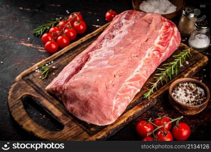 A piece of raw pork on a cutting board with tomatoes, spices and rosemary. On a rustic dark background. High quality photo. A piece of raw pork on a cutting board with tomatoes, spices and rosemary.