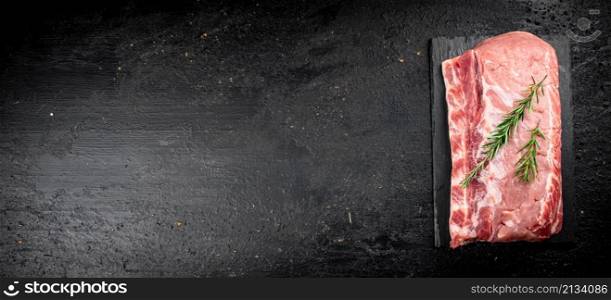 A piece of raw pork on a stone board with a sprig of rosemary. On a black background. High quality photo. A piece of raw pork on a stone board with a sprig of rosemary.