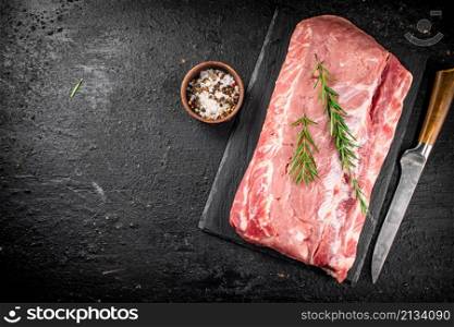 A piece of raw pork on a stone board with a sprig of rosemary. On a black background. High quality photo. A piece of raw pork on a stone board with a sprig of rosemary.