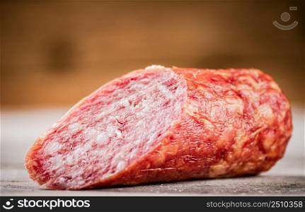 A piece of salami sausage on the table. On a wooden background. High quality photo. A piece of salami sausage on the table.
