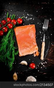 A piece of salted salmon with tomatoes and greens on a stone board. On a rustic with a dark background. High quality photo. A piece of salted salmon with tomatoes and greens on a stone board.