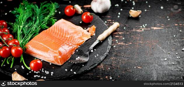 A piece of salted salmon with tomatoes and greens on a stone board. On a rustic with a dark background. High quality photo. A piece of salted salmon with tomatoes and greens on a stone board.