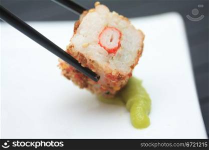 A piece of seame seed sushi and a pair of chopsticks