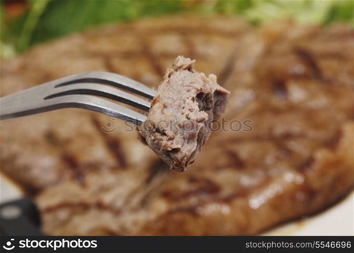 A piece of steak on a fork with a low-carb steak and salad meal in the background