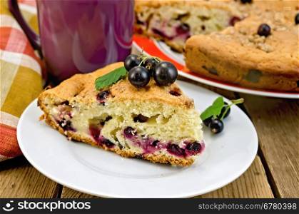 A piece of sweet cake with black currant, napkin, cup on the background of wooden boards