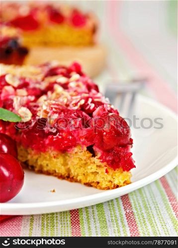 A piece of sweet cake with cherries on a plate against the background of a linen tablecloth