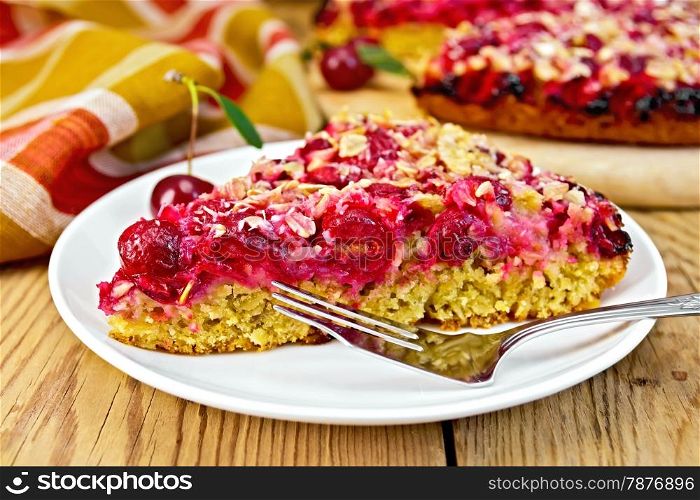A piece of sweet cake with cherries on a plate, napkin, fork on a wooden boards background