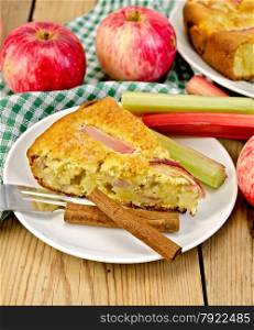 A piece of sweet cake with rhubarb and apples, cinnamon, napkin on a wooden boards background