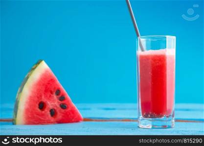 a piece of watermelon and smoothie,freshly squeezed watermelon juice in a transparent glass on a blue wooden background