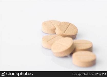 A pile of beige medical tablets on a light background. The blurred part of the image with reflection. Isolated. tablets on a light background
