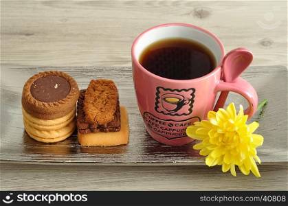 A pile of biscuits with a pink mug filled with coffee and a yellow flower