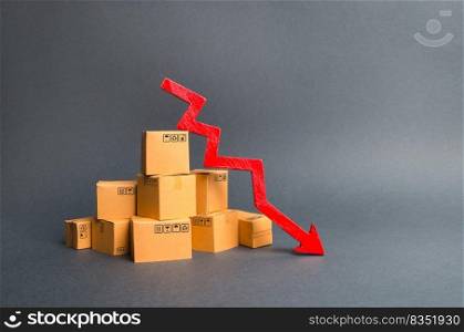 A pile of cardboard boxes and a red arrow down. The decline in the production of goods and products, the economic downturn and recession. Falling consumer demand, declining exports or imports.