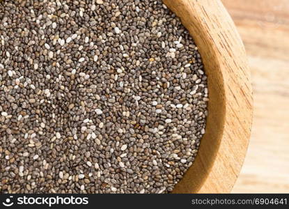 A pile of Chia Seeds in wood bowl on cutting board.