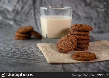 A pile of cookies and a glass of milk on a cloth on a wooden table