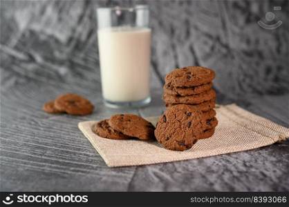 A pile of cookies and a glass of milk on a cloth on a wooden table