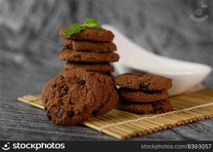 A pile of cookies and a spoon of milk on a cloth on a wooden table