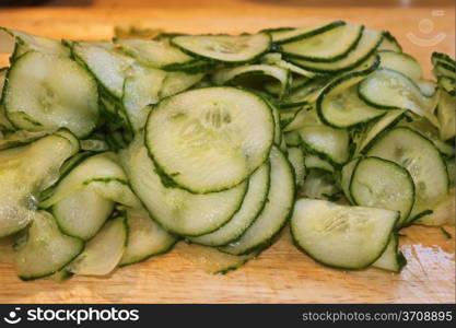 A pile of cut sliced green cucumbers on a wooden board.
