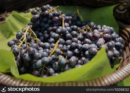A pile of fresh organic ripe sweet juicy black seedless grapes in the wicker basket.