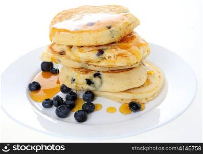 A pile of homemade American-style blueberry pancakes topped with syrup and served with a scattering of the berries.