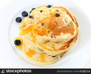 A pile of homemade American-style blueberry pancakes topped with syrup and served with a scattering of the berries, seen from a high angle.