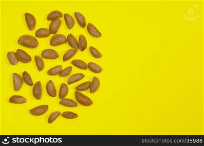 A pile of in shell raw almond on yellow background with copy space