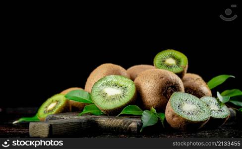 A pile of kiwi with leaves on a cutting board. On a black background. High quality photo. A pile of kiwi with leaves on a cutting board.