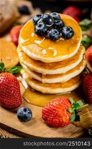 A pile of pancakes with fresh berries and honey on the table. On a wooden background. High quality photo. A pile of pancakes with fresh berries and honey on the table.