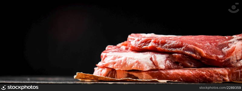 A pile of raw pork steak on the table. On a black background. High quality photo. A pile of raw pork steak on the table.