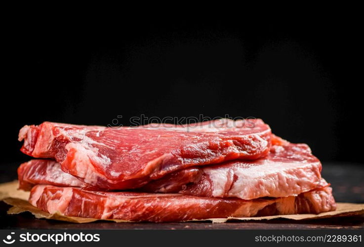 A pile of raw pork steak on the table. On a black background. High quality photo. A pile of raw pork steak on the table.