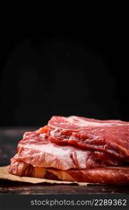 A pile of raw pork steak on the table. On a black background. High quality photo. A pile of raw pork steak on the table.