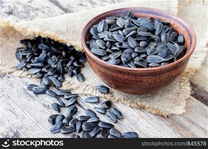 A pile of sunflower seeds in a bowl on a wooden background. Sunflower seeds scattered on the table. Close-up.. A pile of sunflower seeds in a bowl on a wooden background. Sunflower seeds scattered on the table.