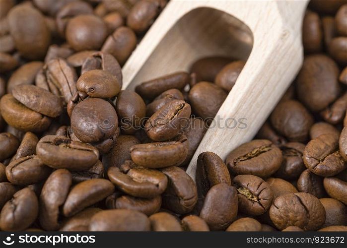 a pile of whole roasted coffee beans, close-up of a wooden spoon or scoop with grains inside. coffee beans